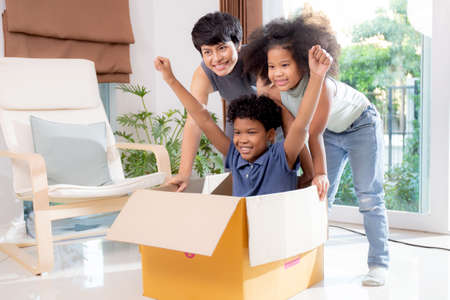 Happiness African family with mother and daughter pushing cardboard box with inside son excited...