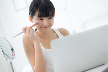 Beauty of young asian woman with learning makeup with brush on cheek on laptop computer with tutorial course online, female teaching and explain make up with cosmetic on streaming social media.の写真素材