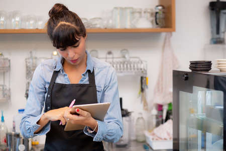 Young woman is barista using tablet computer for order delivery online in the cafe, entrepreneur and...