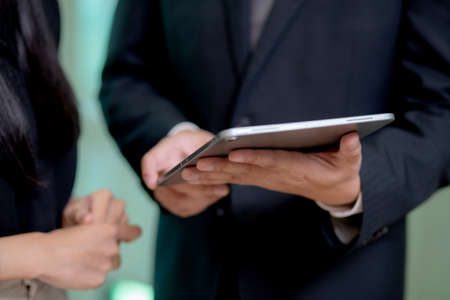 Closeup hands of business team man and woman standing and talking about marketing on tablet with social network at the office, secretary report with executive for planning marketing, business concept.の写真素材