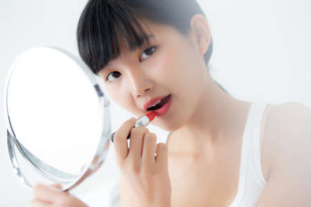 Beautiful young asian woman applying lipstick red on mouth, beauty girl looking facial at mirror for makeup cosmetic with lips elegance, make up with sexy of female, skin care and health concept.の写真素材