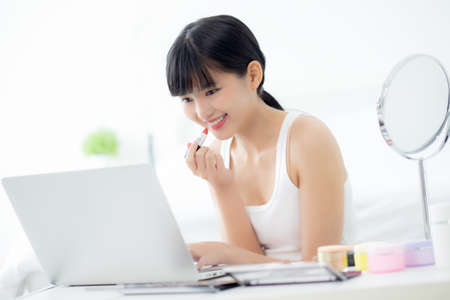 Beauty of young asian woman with learning makeup with lipstick on mouth watching laptop computer with tutorial course online, female teaching and explain make up with cosmetic on streaming media.の写真素材