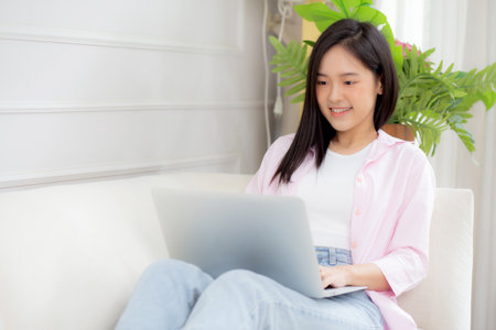 Young asian business woman work from home with laptop computer online to internet on sofa in living room, freelance girl using notebook sitting on couch with comfort and relax, lifestyles concept.の写真素材