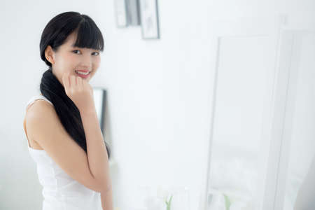 Beautiful face of young asian woman with happy smiling and touch cheek looking mirror with charming,...