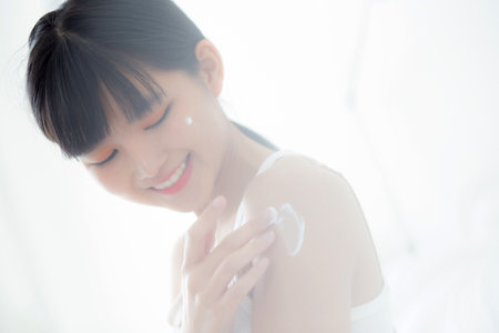 Beautiful young asian woman happy applying cream or lotion with moisturizer to skin on shoulder, beauty asia girl applying skincare with cosmetic makeup for hygiene and wrinkle, skin care concept.の写真素材