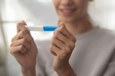 Happiness young asian woman taking pregnancy test while excited and satisfied in the bedroom at home, happy mother with smile and expression with love, ovulation and maternity, medical concept.の写真素材