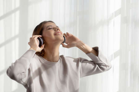 Happy young asian woman wearing headphones listening music while dancing and singing with fun and...