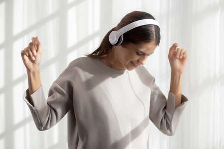 Happy young asian woman wearing headphones listening music while dancing and singing with fun and...