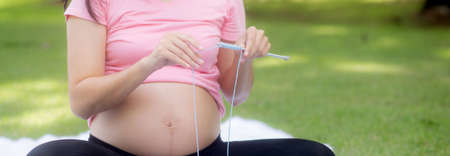 Happiness young asian woman pregnant sitting doing knit hat with for relaxation in the park, mother...