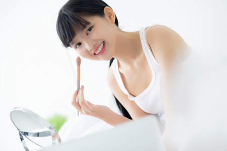 Beauty of young asian woman with learning makeup with brush on cheek on laptop computer with tutorial course online on bed, female teaching and explain make up with cosmetic on streaming social media.の写真素材