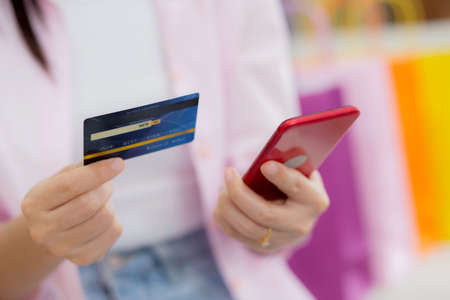 Hands of woman sitting on sofa using smart phone shopping online with credit card while paper bag on couch, happy female paying with transaction financial, purchase and payment, business concept.の写真素材