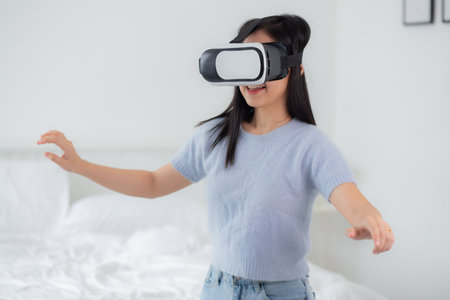 Young asian woman wearing vr headset playing game with excited in the bedroom at home, female using virtual reality or metaverse innovation for simulation 3D, lifestyles and technology concept.の写真素材