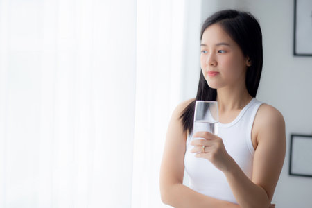 Beautiful young asian woman drinking glass of water mineral pure with fresh and happy at home, asia female drinking beverage for healthcare and weightloss, one person, lifestyles concept.の写真素材