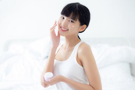 Beautiful young asian woman holding cartridge applying cream or lotion with moisturizer to skin on face, beauty asia girl applying skincare touch facial with cosmetic makeup, skin care concept.の写真素材