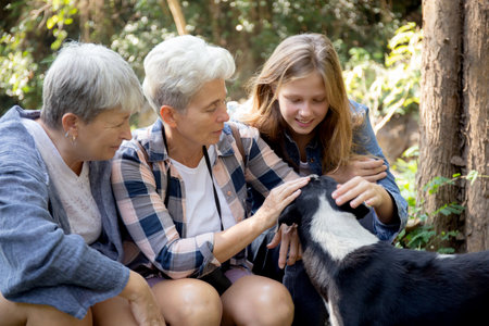 Teenager girl and two grandmother traveling travel to forest and adventure while playful with dog together with happy, senior woman and granddaughter hiking with fun and vitality in holiday.の写真素材