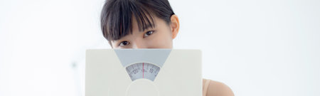 Portrait of beautiful young asian woman holding scales with confident with control and weightloss, girl dieting for result of weight loss with satisfied, one person, healthy and lifestyles concepts.の写真素材