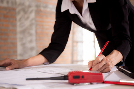 Closeup hands young caucasian architect woman looking laptop and working drawing blueprint for...