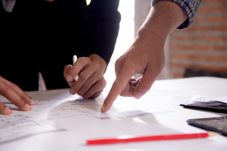 Closeup hands young caucasian architect woman looking laptop and working drawing blueprint for planning building house, engineer thinking and sketching blueprint for construction, industry concept.の写真素材