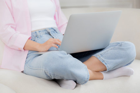 Closeup hands business woman work from home with laptop computer online to internet on sofa in living room, freelance girl using notebook sitting on couch with comfort and relax, lifestyles concept.の写真素材