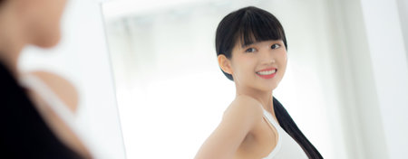 Beautiful young asian woman looking body in mirror with belly figure slim at home, beauty girl shape fit with weight loss, abdomen and waist sexy perfect, weightloss and diet, lifestyles concept.の写真素材