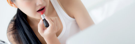 Beauty of young asian woman with learning makeup with lipstick on mouth watching laptop computer with tutorial course online on bed, female teaching and explain make up with cosmetic on streaming.の写真素材