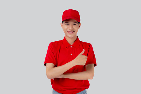 Young asian man in uniform red and cap standing thumbs up with confident isolated on white background, employee or dealer, courier and delivery, deliveryman and expression, logistic and cargo.の写真素材