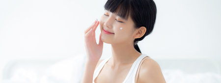 Beautiful young asian woman holding cartridge applying cream or lotion with moisturizer to skin on face, beauty asia girl applying skincare touch facial with cosmetic makeup, skin care concept.の写真素材