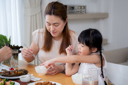 Happiness asian family mother and father and daughter eating food in kitchen together at home, parent and kid sitting dining in living room, bonding and relation, lifestyles and nutrition concept.の写真素材