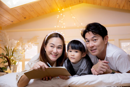 Happy family with mother and father lying teaching homework with daughter on bed in bedroom at home, mom and dad explaining schoolwork with kid with enjoy together, lifestyles and education.の写真素材
