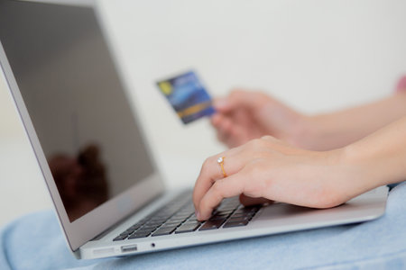 Closeup hands of woman sitting on sofa using laptop computer online shopping with credit card, happy female payment with debit card on couch, purchase and payment, business and technology concept.の写真素材
