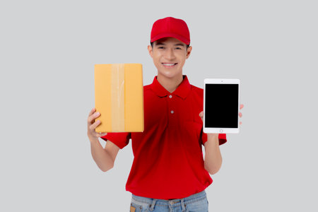 Portrait young asian man in uniform standing holding box or package and digital tablet show and presenting isolated white background, delivery man express and shipping, logistic and cargo.の写真素材