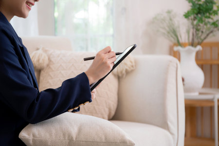 Closeup hands young asian businesswoman sitting on sofa using tablet computer for planning success business in living room at home office, business woman relax while writing on digital tablet.の写真素材