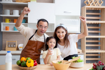 Happy family with father, mother and daughter in kitchen drinking milk in glass for healthy together at home, mom, dad and child with bonding and relation, lifestyles and nutrition concept.の写真素材