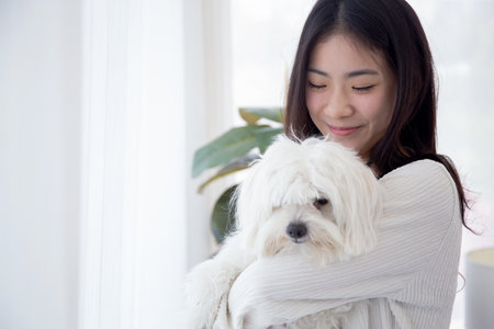 Young asian woman standing carrying with fluffy dog shih tzu with love in living room at home,...