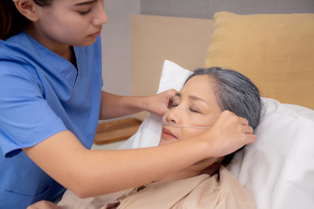 Nurse putting oxygen with patient elderly woman on bed for diagnose and healing in hospital, specialist doctor giving oxygen mask with senior emergency for recovery in clinic, medical concept.の写真素材