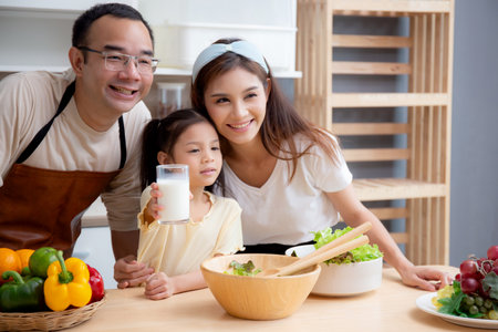 Happy family with father, mother and daughter in kitchen drinking milk in glass for healthy together at home, mom, dad and child with bonding and relation, lifestyles and nutrition concept.の写真素材