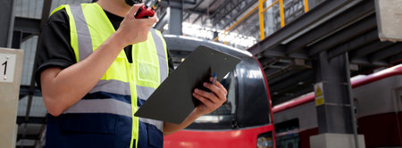 Young caucasian engineer man or worker hold clipboard for looking and checking electric train for planning maintenance and using radio for command in station, inspector check service transport.の写真素材