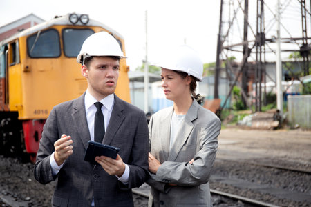 Young caucasian engineer man and woman in suit checking train with tablet in station, team engineer inspect system transport, technician examining infrastructure, transportation and industry.の写真素材