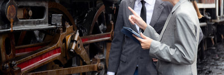 Young caucasian engineer man and woman in suit checking train with tablet in station, team engineer inspect system transport, technician examining infrastructure, transportation and industry.の写真素材