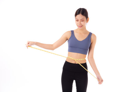 Portrait beautiful young asian woman measure tape with waist for weightloss with satisfied isolated white background, female in sportswear slimming shape with workout, sport and health care concept.の写真素材