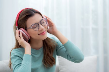 Happy young woman wearing headphones listening music while sitting on sofa with fun and enjoy in the living room at home, happiness female with entertainment, one person, lifestyle concept.の写真素材