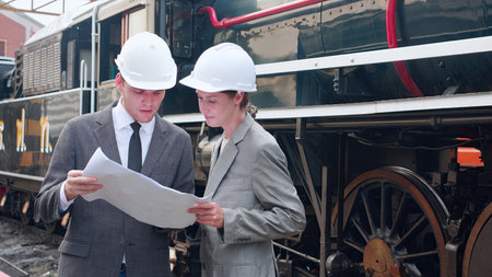 Young caucasian engineer man and woman in suit checking train looking blueprint in station, team engineer inspect system transport, technician examining infrastructure, transportation and industry.の写真素材