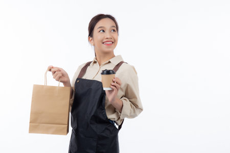 Young asian woman barista work attire happy holding a takeaway coffee cup and paper bag isolated...