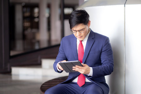 Professional young asian businessman in suit using tablet while sitting in modern office, business man looking on tablet for planning finance with concentration, business and communication.の写真素材