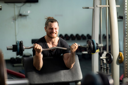 Man working out in a gym, lifting weights with a focused and intense expression, showcasing strength...
