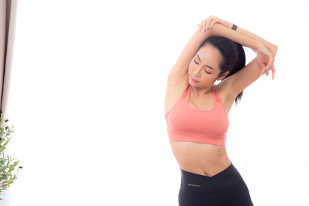 Beautiful young asian woman standing workout with warmup and stretch muscle arm and hands at home, female exercise for relax with sport, motivation and determined for health, sport concept.の写真素材