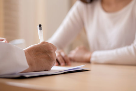 Senior woman doctor consults with young patient in modern medical office, doctor explaining and diagnosis with patient about health and treatment while writing on notes, medical and insurance.の写真素材