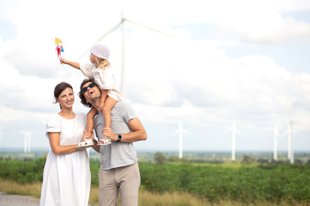 Happiness family walking wind turbine farm while father piggyback of daughter together, environment and energy of sustainability, resource nature and sustainable, environment and bonding of family.の写真素材