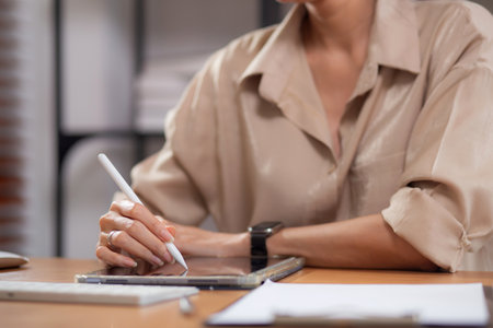 Closeup hand young businesswoman using tablet while writing on desk in living room at modern home office, business woman using tablet, entrepreneur or freelance, business and commercial.の写真素材