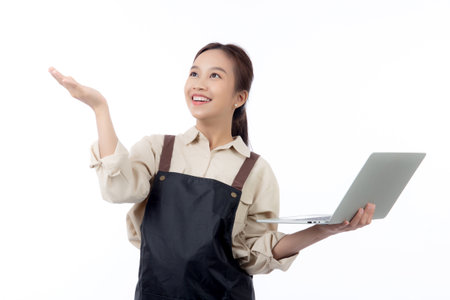 Portrait young asian business woman wearing apron holding laptop computer isolated white background, waitress or barista holding laptop computer with success, cut out, business or freelance.の写真素材